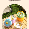 A set of yellow and green insulated stainless steel breakfast cups with lids placed on a wooden table outdoors.
