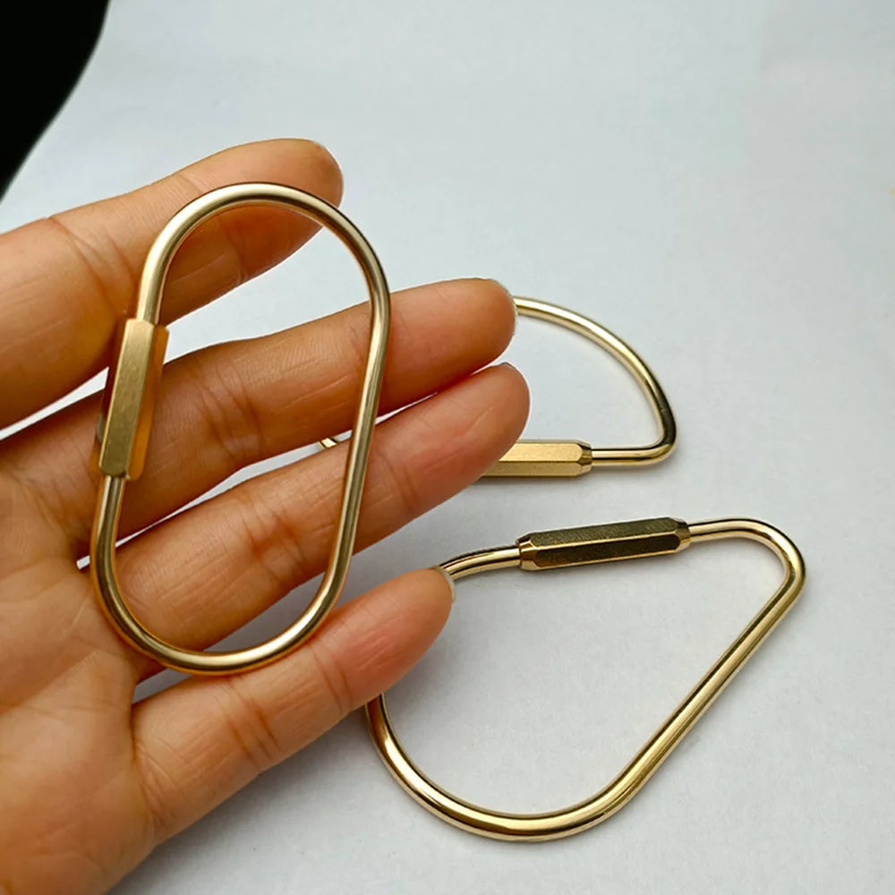 A hand holds a brass keychain with a locking carabiner clip.