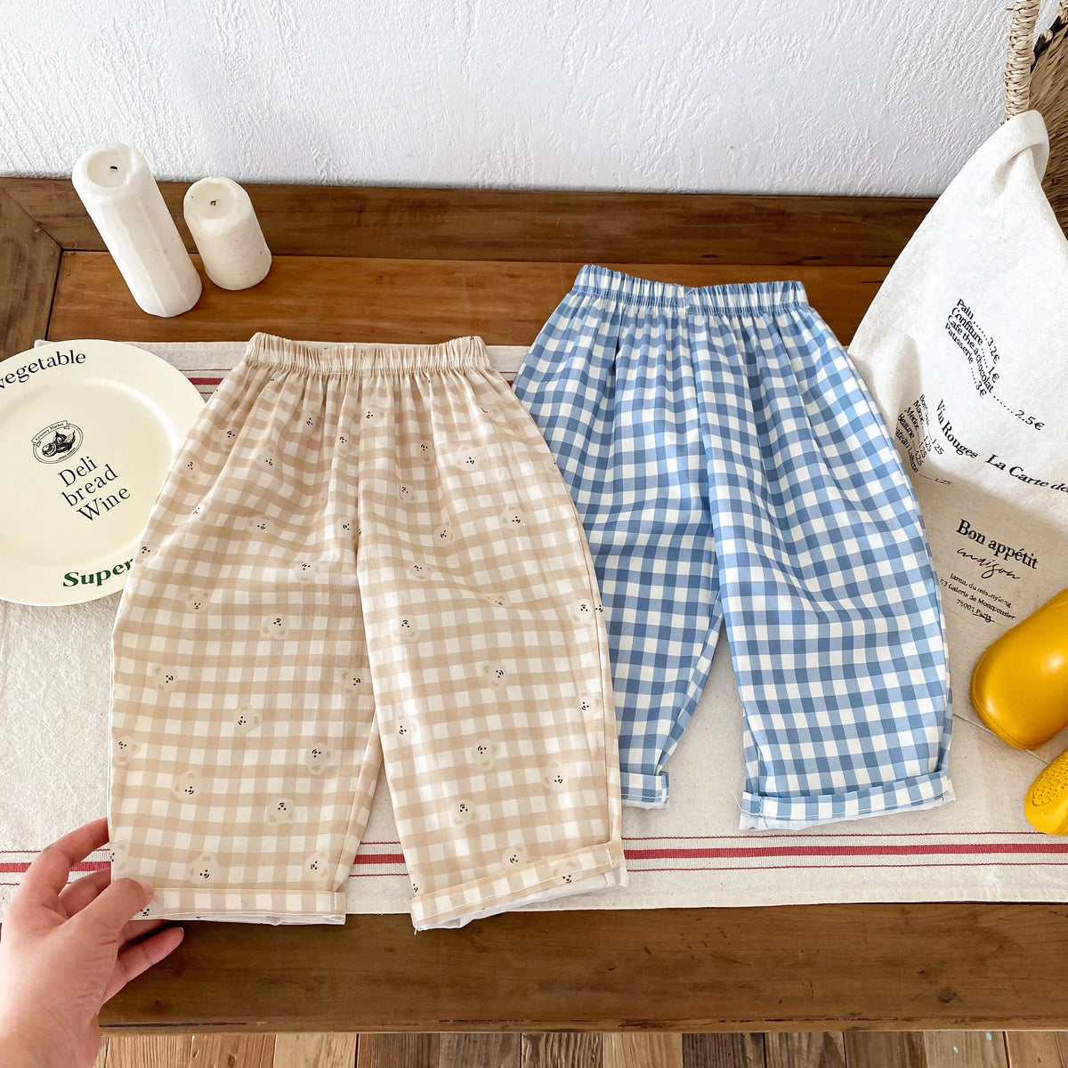A pair of light beige plaid print casual pants with an elastic waist laid out on a wooden surface.