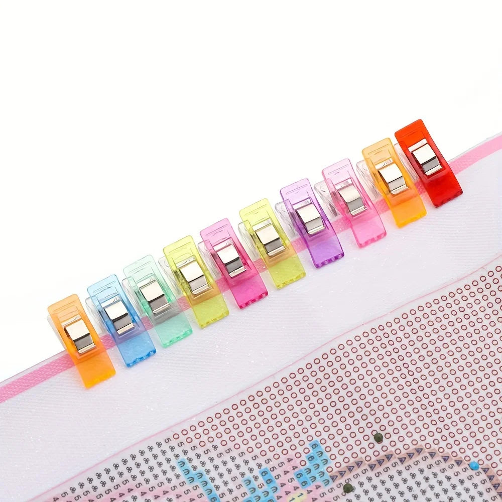 An array of eight diamond painting clips in various colors, including orange, pink, and yellow, arranged diagonally on a whit