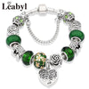 Silver charm bracelet featuring green leaf and floral accents, including a tree of life pendant.