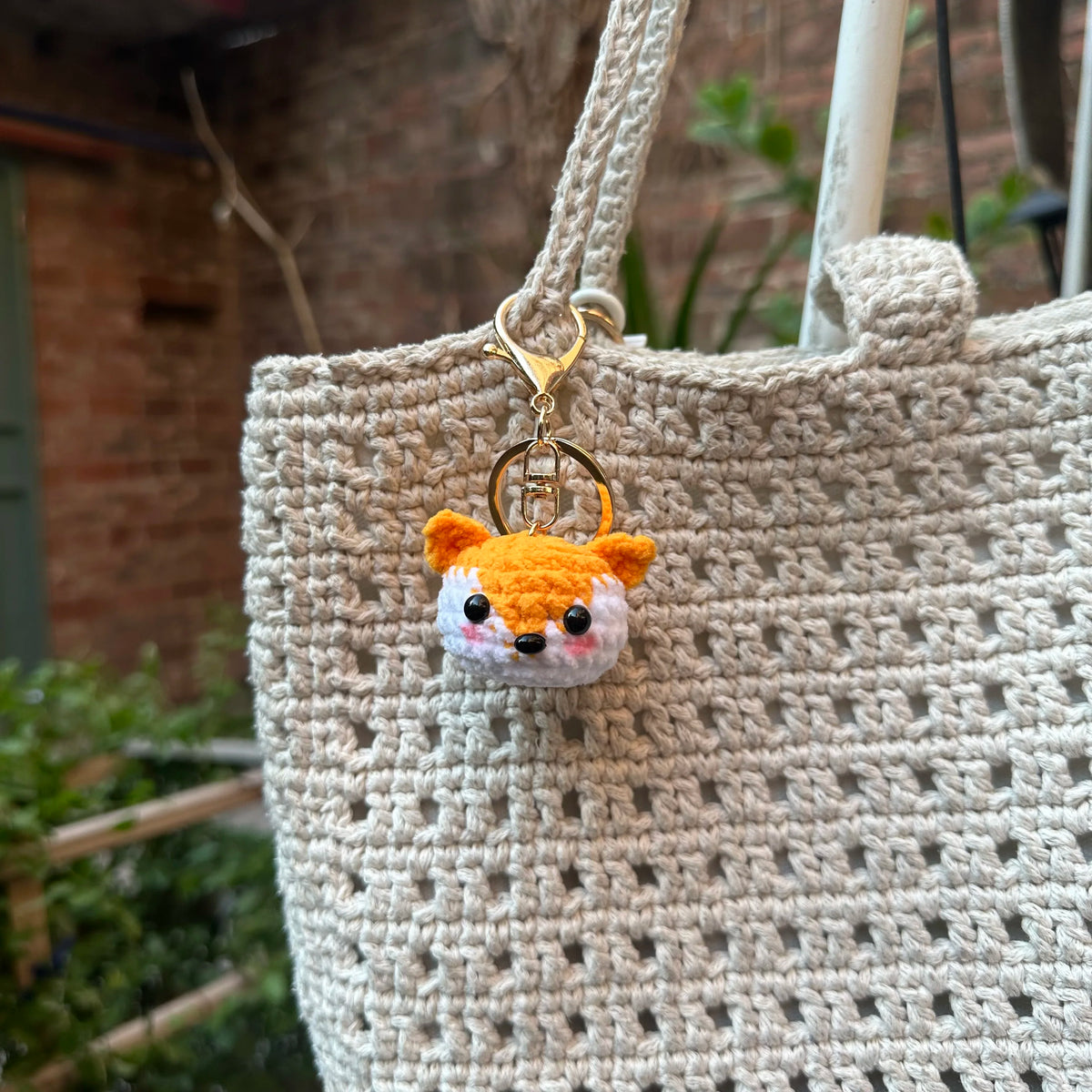 A handcrafted crochet animal keychain featuring a small orange and white rabbit face attached to a beige woven bag.