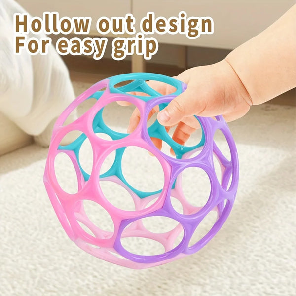 A hand is gripping a colorful, hollow out design sensory ball for infants.
