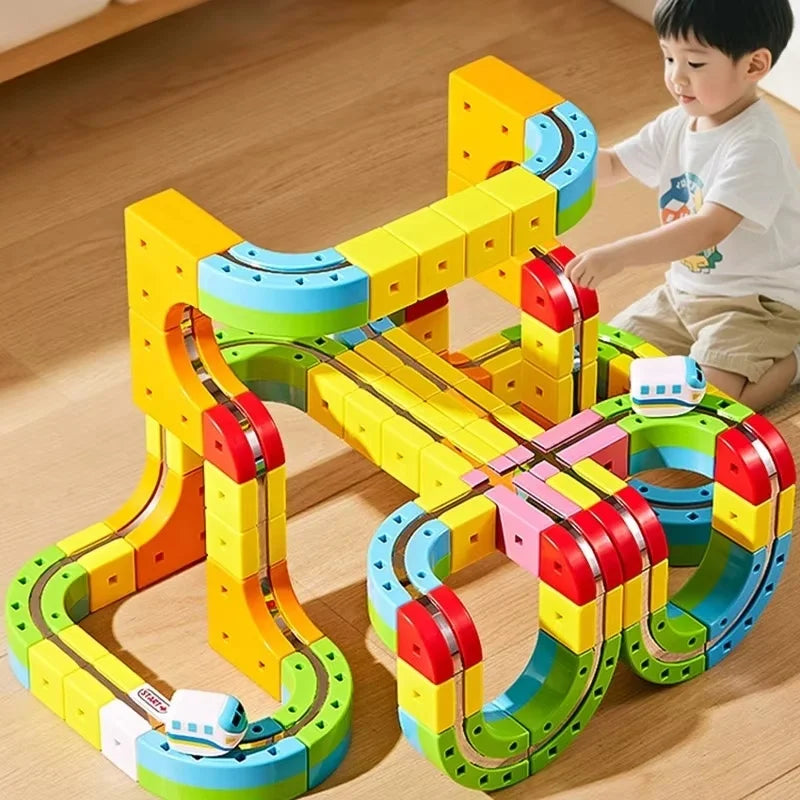 A child is playing with a yellow and blue magnetic track train set made of flexible plastic pieces on a wooden floor.