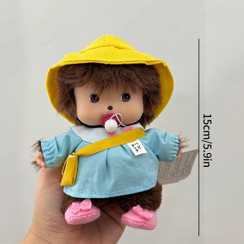 A yellow hat plush cartoon character wearing a blue shirt and gold strap, held by a hand.