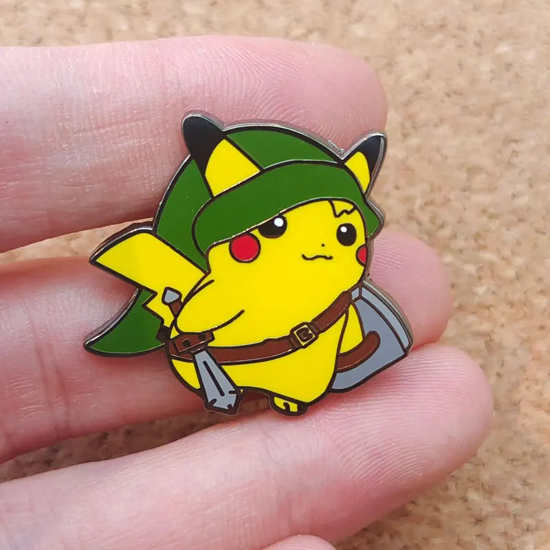 A yellow Pokémon enamel pin featuring a green hat and brown belt, held by a person's fingers.