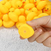 A hand holds a yellow rubber duck from a set of mini rubber ducks on a white surface.
