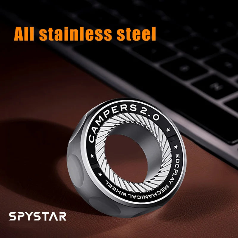 A silver magnetic fidget ring called SPYSTAR is shown on a dark surface next to a laptop keyboard.