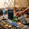 A hand holds a deck of Mystical Moon Oracle cards surrounded by crystals, herbs, and incense on a richly patterned cloth.