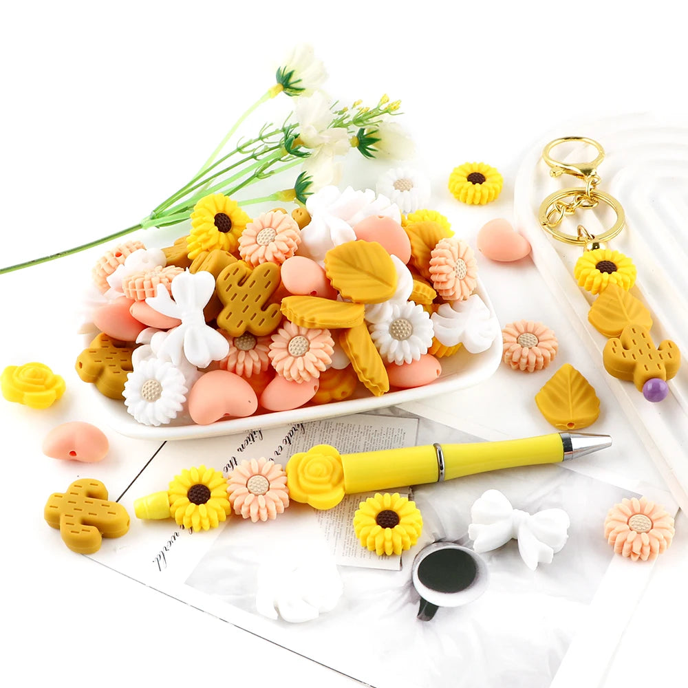 A collection of yellow, pink, and white silicone flower and leaf beads used for jewelry making, displayed on a white plate.