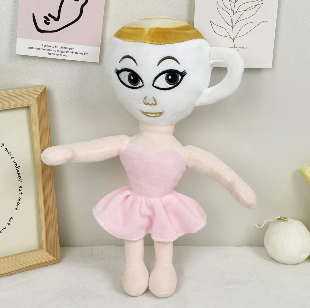 A white and gold plush toy shaped like a mug with a face, standing in front of framed text.