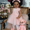 A toddler doll with hand-rooted black hair wearing a pink dress sitting on a chair.