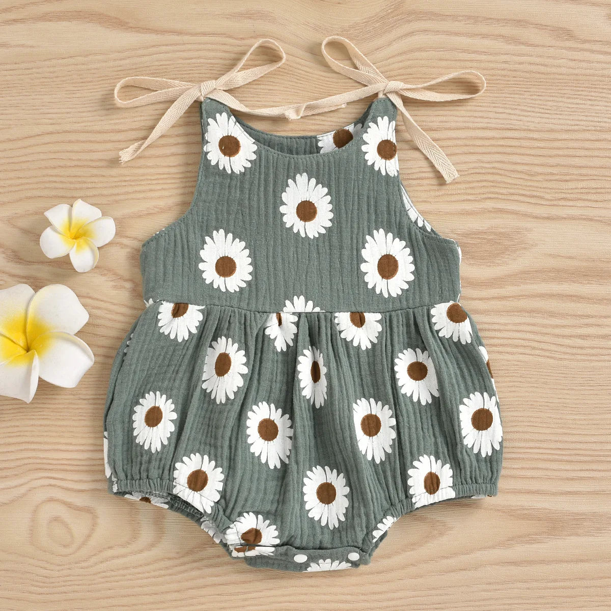 A gray cotton romper for a baby girl with a white daisy floral print, tied at the shoulders.