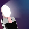 A portable LED selfie ring light is clipped onto a smartphone, illuminating the area.