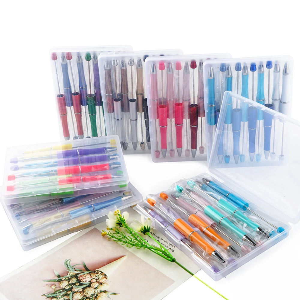 A collection of DIY beaded ballpoint pen kits in clear plastic containers and a wooden surface.
