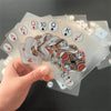A hand holds a stack of waterproof transparent playing cards featuring Ace, King, Queen, and Ten cards.