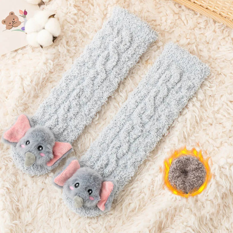 Gray plush baby knee-high socks with pink ears and a glowing charm resting on a fluffy white background