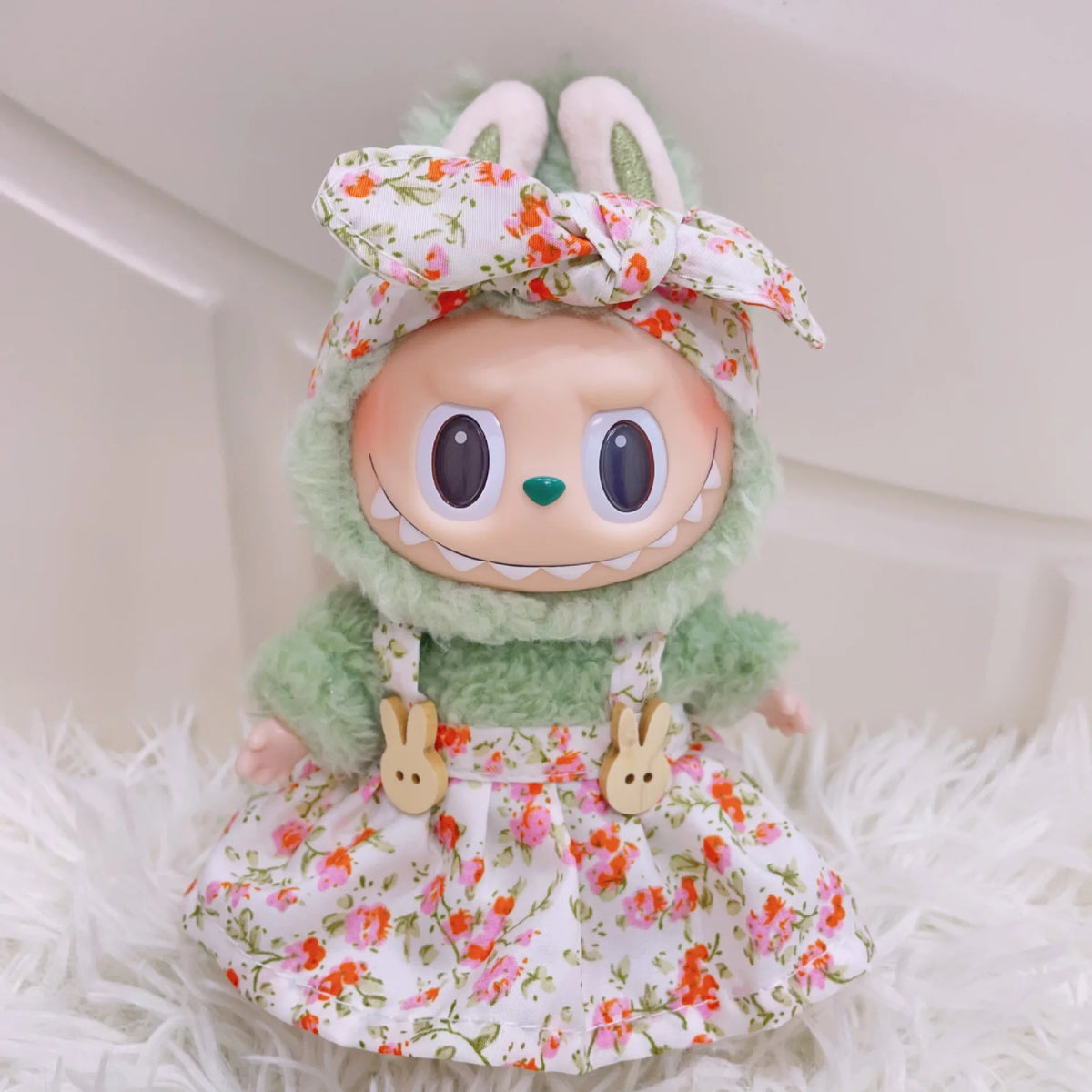 A doll wearing a floral dress and headband, sitting on white fluffy material.