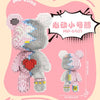 A pink brick art bear figure made of building blocks with a heart detail and yellow accents.