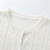 A close-up of a white knitted cotton cardigan with a ribbed collar and button closure.