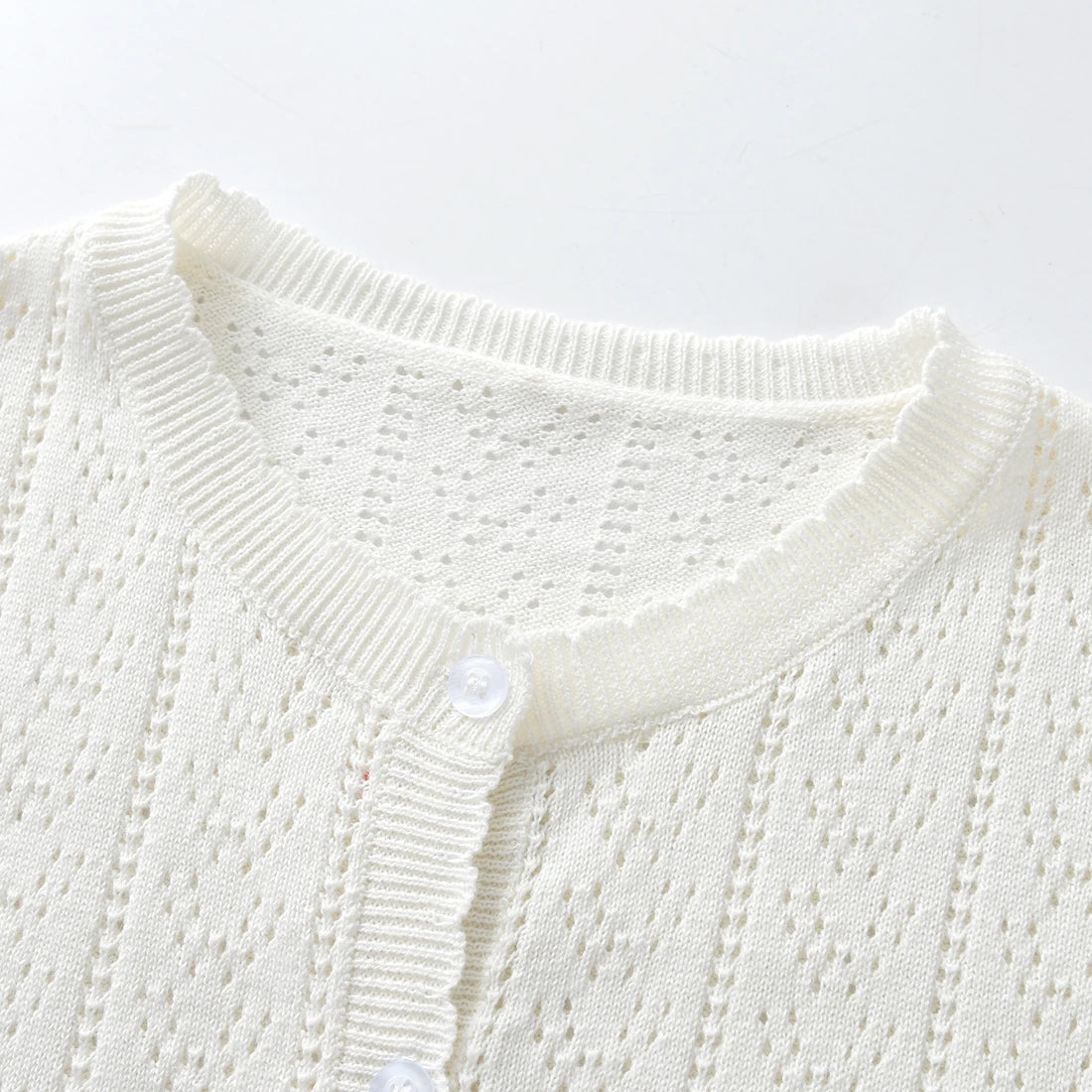 A close-up of a white knitted cotton cardigan with a ribbed collar and button closure.