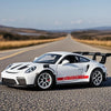 A white Porsche 911 GT3 RS diecast model car is parked on an asphalt road with a scenic landscape in the background.