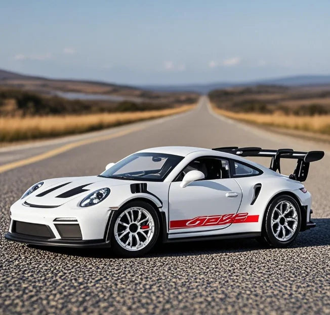 A white Porsche 911 GT3 RS diecast model car is parked on an asphalt road with a scenic landscape in the background.