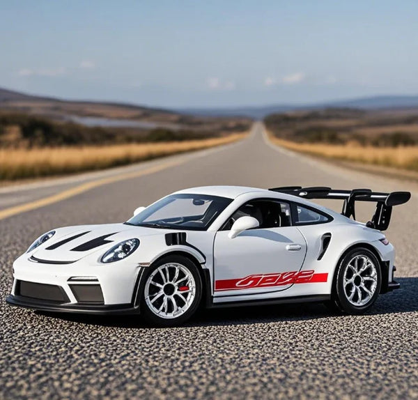 A white Porsche 911 GT3 RS diecast model car is parked on an asphalt road with a scenic landscape in the background.