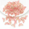 A pile of pink and green butterfly glass beads for jewelry making on a white dish.