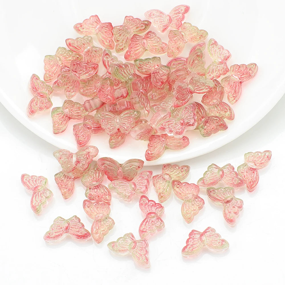 A pile of pink and green butterfly glass beads for jewelry making on a white dish.