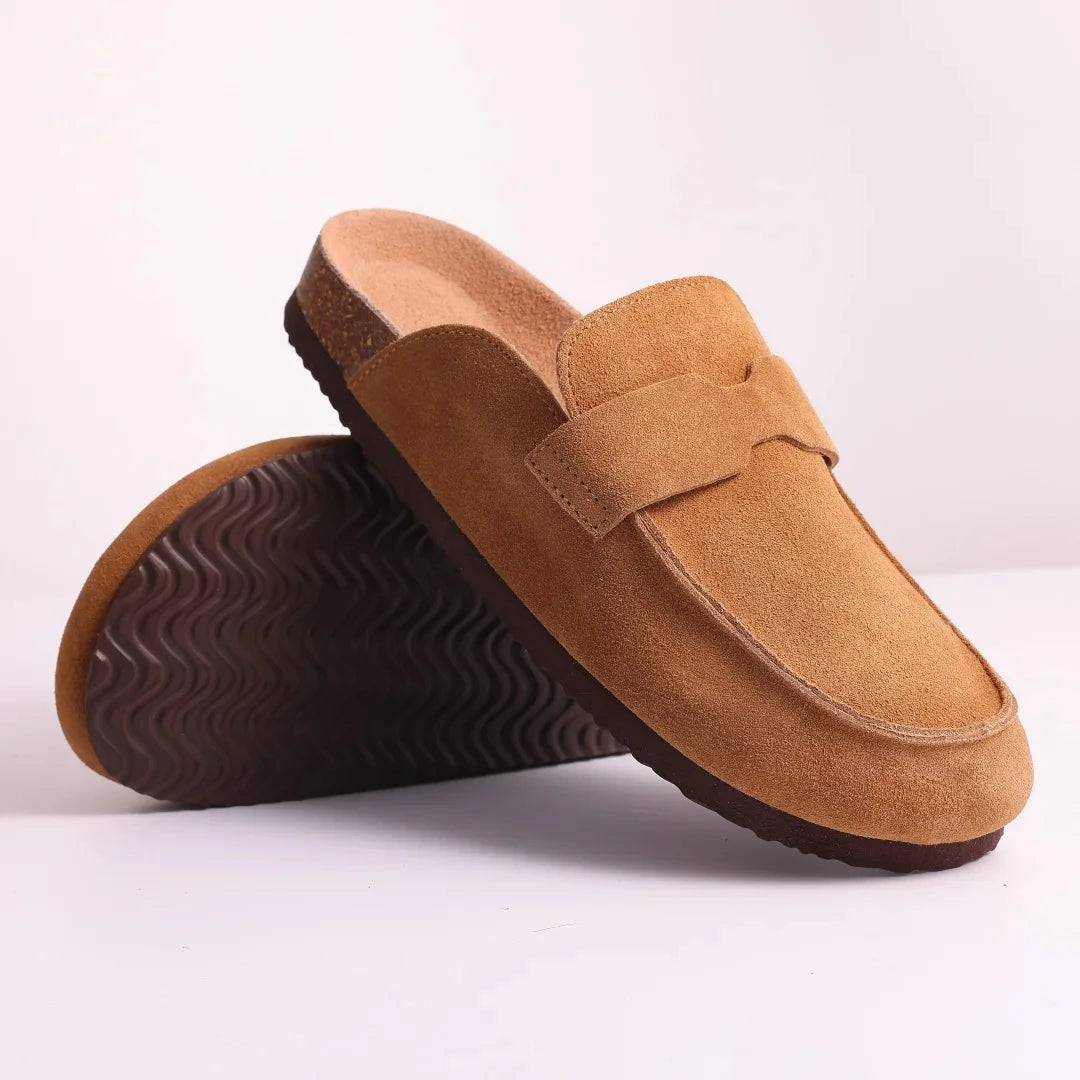 A pair of brown suede cork mules with arch support shown from the side.