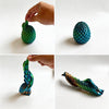 A hand holds a textured, teal dragon egg fidget toy, showing its intricate scale pattern from different angles.