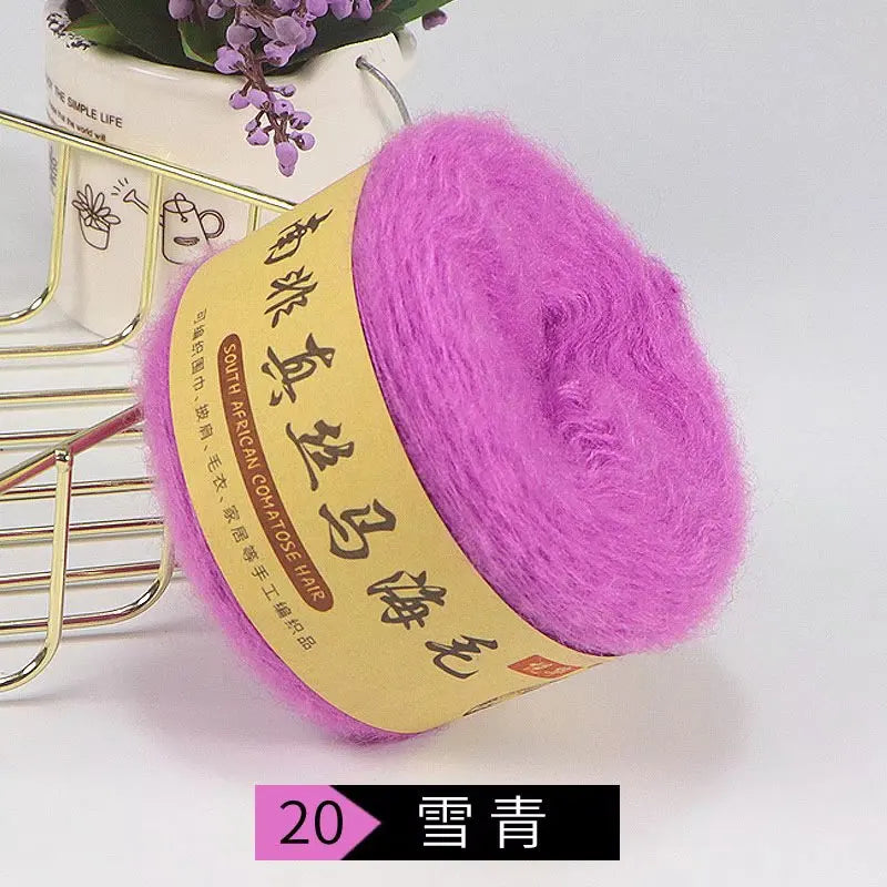 A ball of bright pink mohair blended yarn is displayed next to a gold-colored knitting tool.