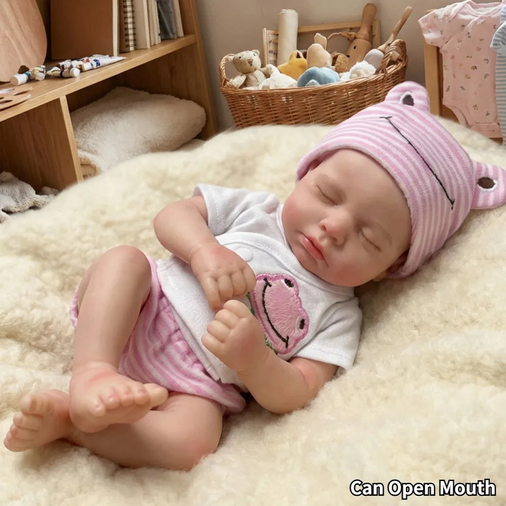 A realistic reborn baby doll with pink knitted hat and clothing lying on a fluffy white surface.