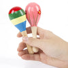 A hand holds a wooden sand hammer percussion instrument with colorful painted heads.