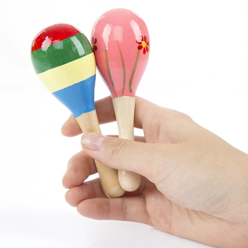 A hand holds a wooden sand hammer percussion instrument with colorful painted heads.
