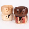 A pair of handcrafted wooden yarn bowls with swirl cutouts, showing light and dark wood tones.