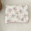 A white cotton muslin swaddle blanket with a pink floral print laid flat on a light background.