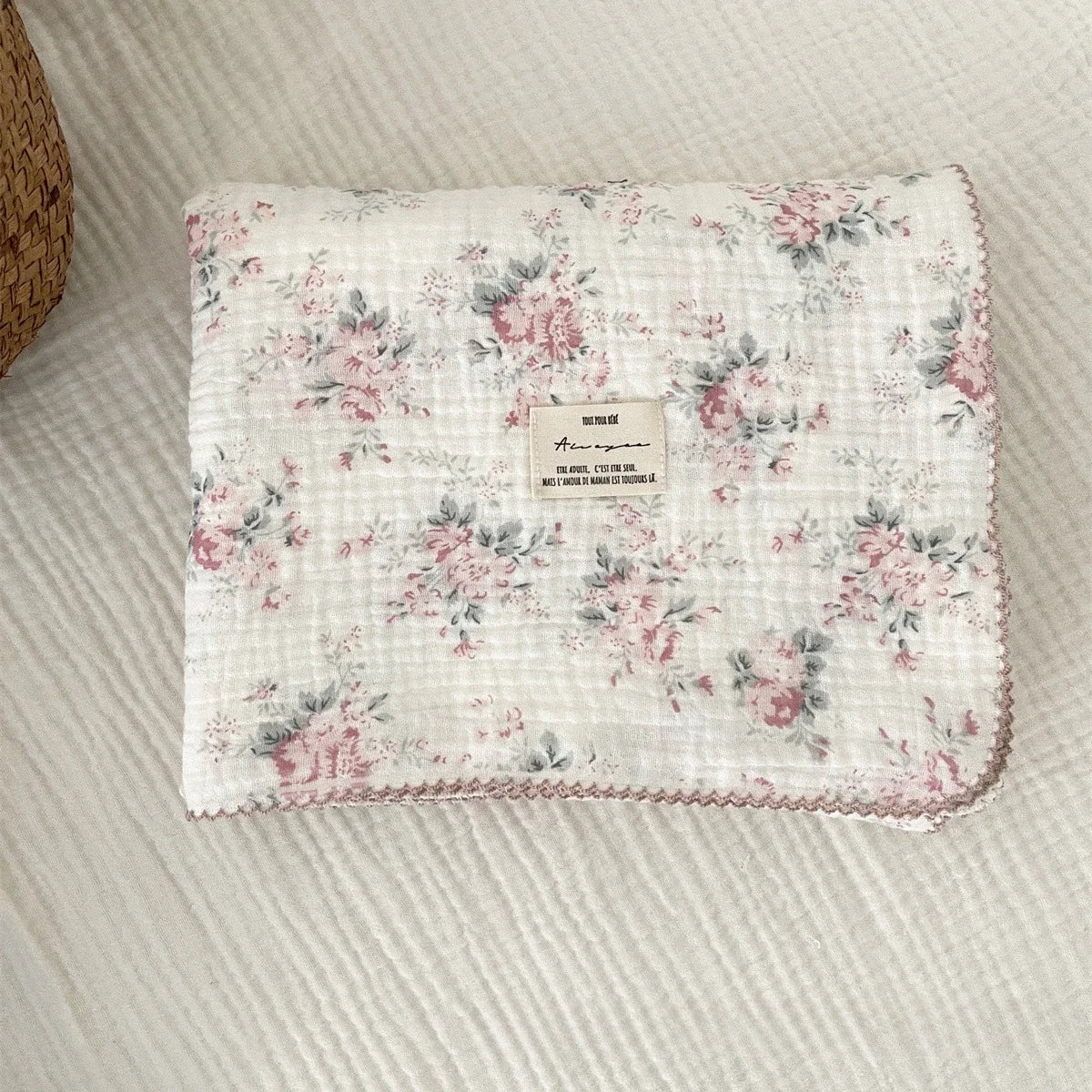A white cotton muslin swaddle blanket with a pink floral print laid flat on a light background.