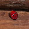 An enamel lapel pin depicting a stylized, distressed face with intense eyes and open mouth on a wooden surface.
