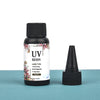 A small glass bottle of UV resin glue with a black cap and a separate applicator tip is shown on a teal surface.