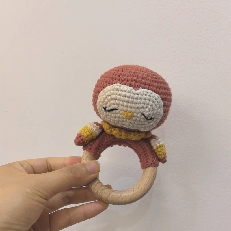 A handmade wooden baby rattle and teether ring featuring soft reddish-brown yarn and a cute face design.