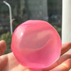 A hand holds a translucent pink squishy stress ball with gentle swirling patterns.