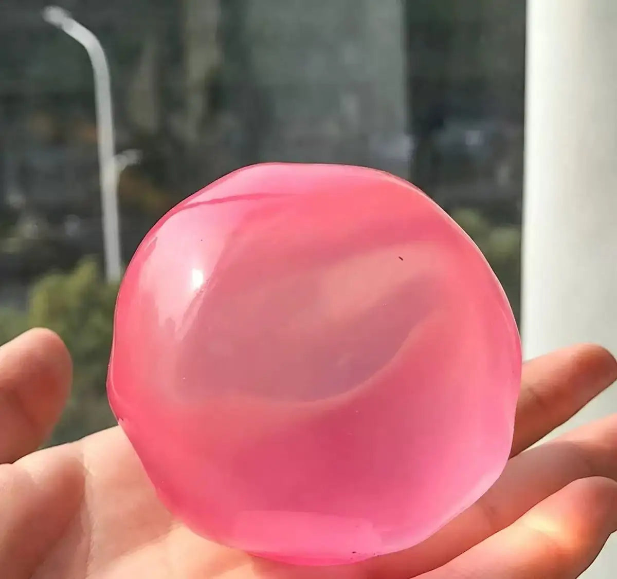 A hand holds a translucent pink squishy stress ball with gentle swirling patterns.