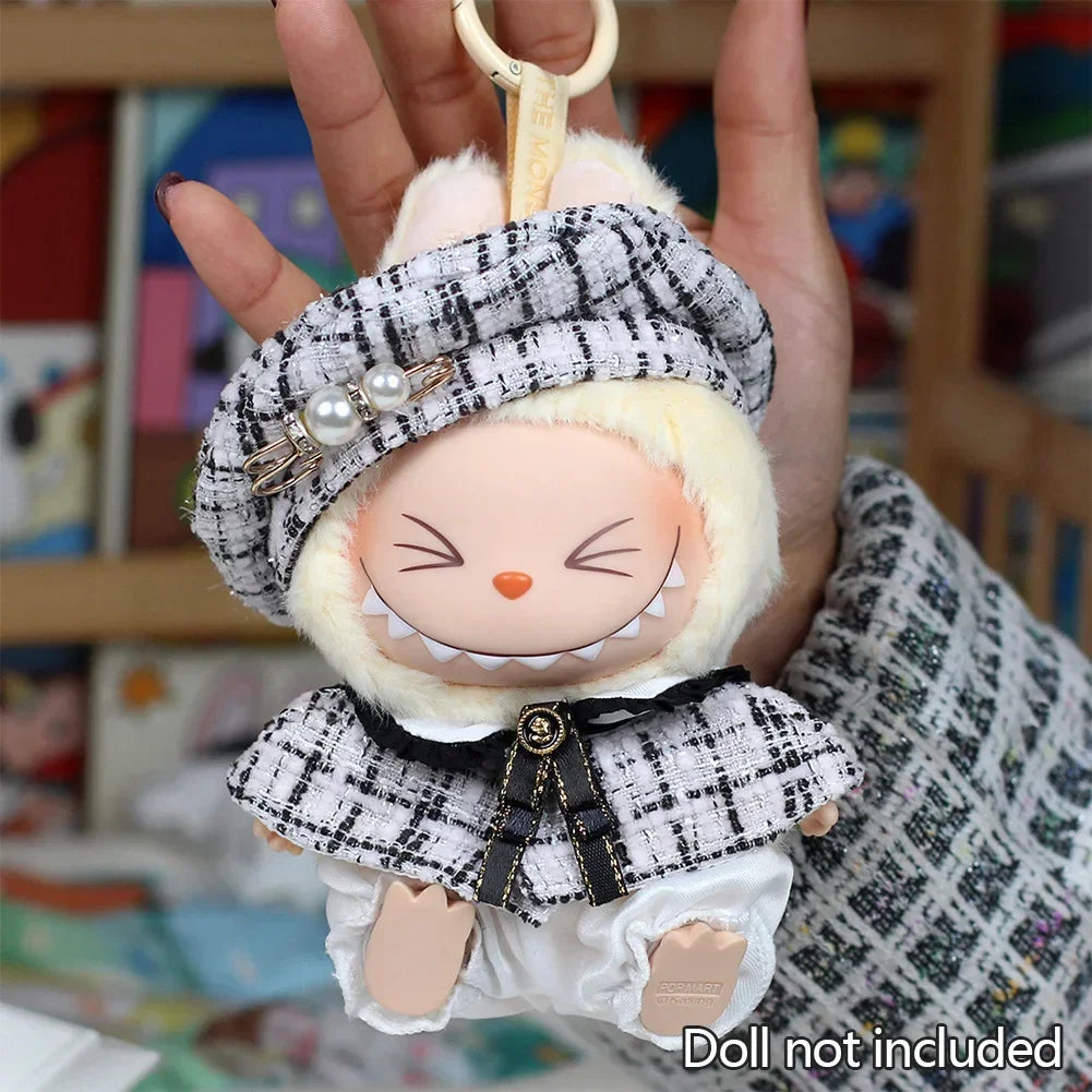 A handmade doll wearing a gray grid cape and beret with white fur trim and pearl accents.