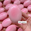 A hand holds a pink squishy cheese cake stress relief toy with many similar toys in the background.