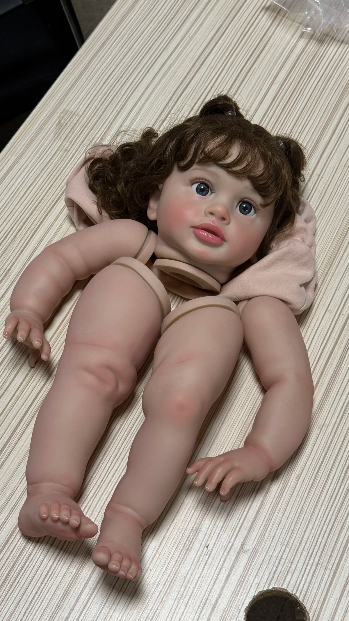 A lifelike reborn baby doll kit with painted vinyl parts, featuring brown hair and blue eyes.