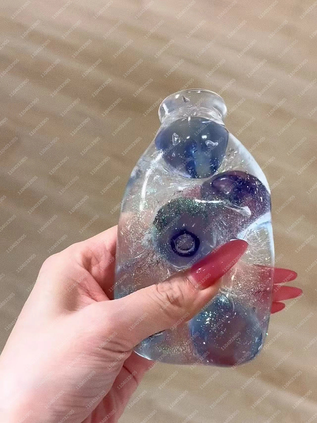 A hand holds a clear glass bottle filled with purple and blue squishy fruit toys.