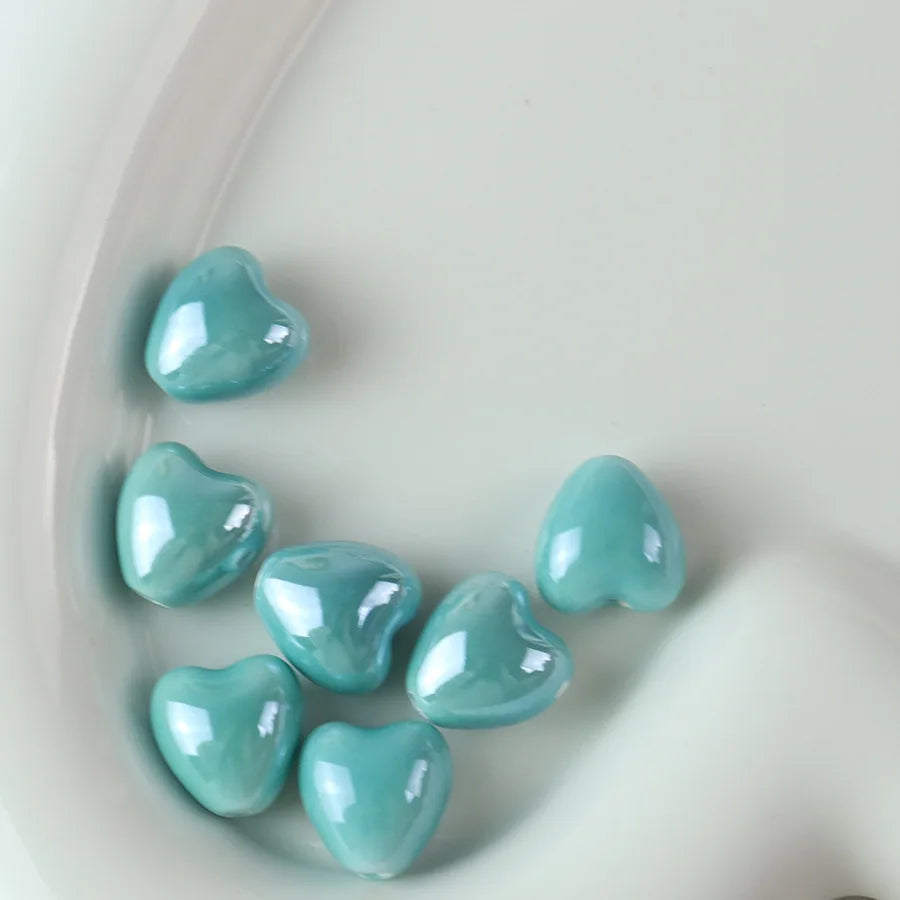 A collection of light blue heart-shaped ceramic beads scattered on a white surface.