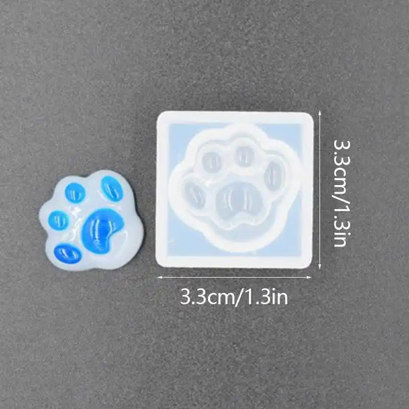 A white silicone mold shaped like a bear paw print with blue silicone inserts for resin jewelry and crafts.